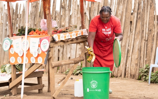 "A woman, Serah Wambui, throws waste into a FoodFiti-branded bin as part of a food safety awareness initiative.