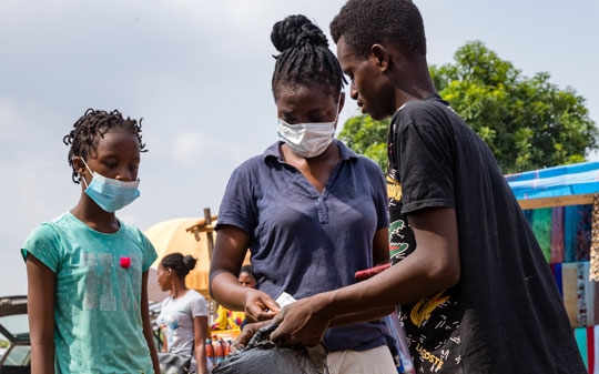 Woman and girl buying food from a man in Nigeria next to a car