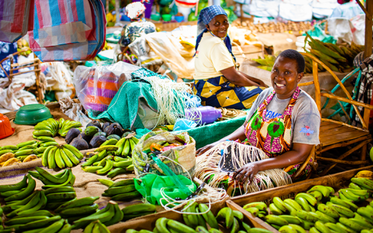 a woman selling bananas and other vegetables